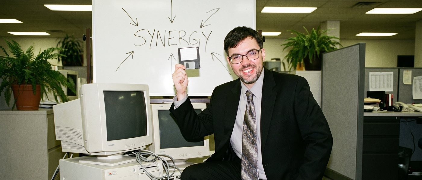 Jeff holding up a floppy disk under a SYNERGY whiteboard
